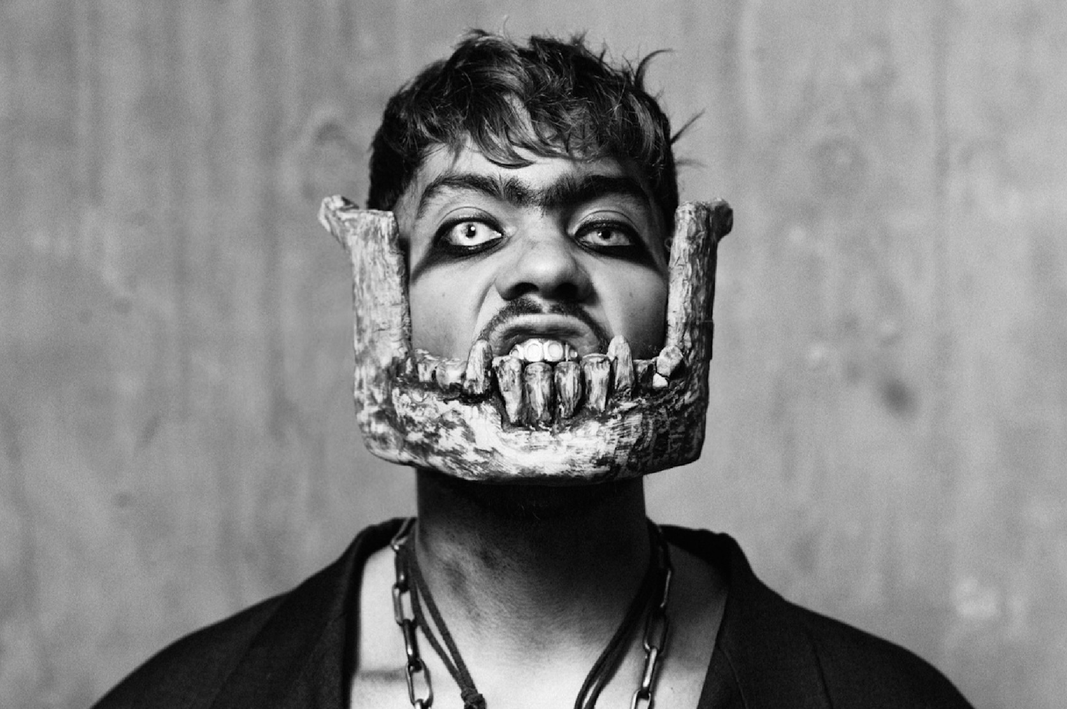 The musician Cain Culto is styled in an avant garde look with half an animal skull resting on his jawline and a dramatic black eye makeup look.